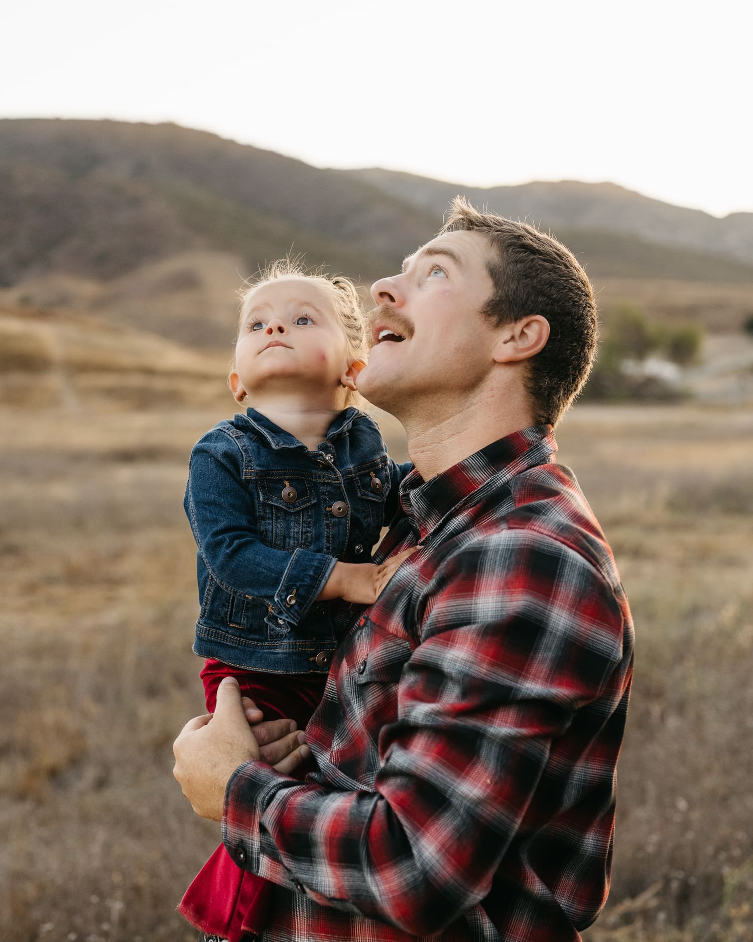 Father holding daughter while both looking up at the sky in a desert setting.