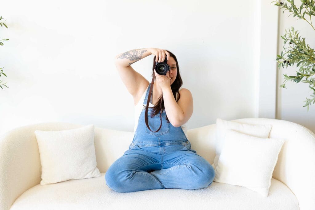 kim kuehn photographer sitting on a white couch posing taking a picture of the photographer